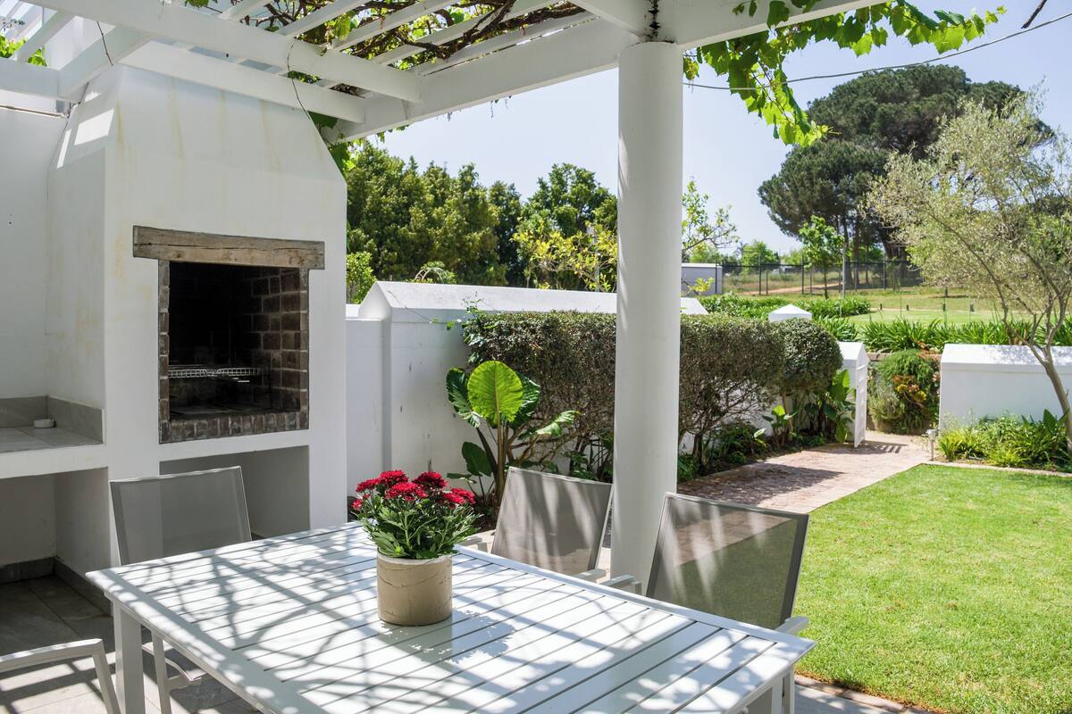Une terrasse extérieure avec un barbecue, une table blanche, des chaises et une plante en pot.