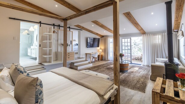 Um quarto espaçoso com uma cama grande, vigas de madeira, uma escrivaninha e uma lareira.