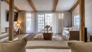 Uma sala de estar ampla com teto de madeira, uma grande janela com cortinas, uma mesa redonda de madeira com uma planta e um sofá.