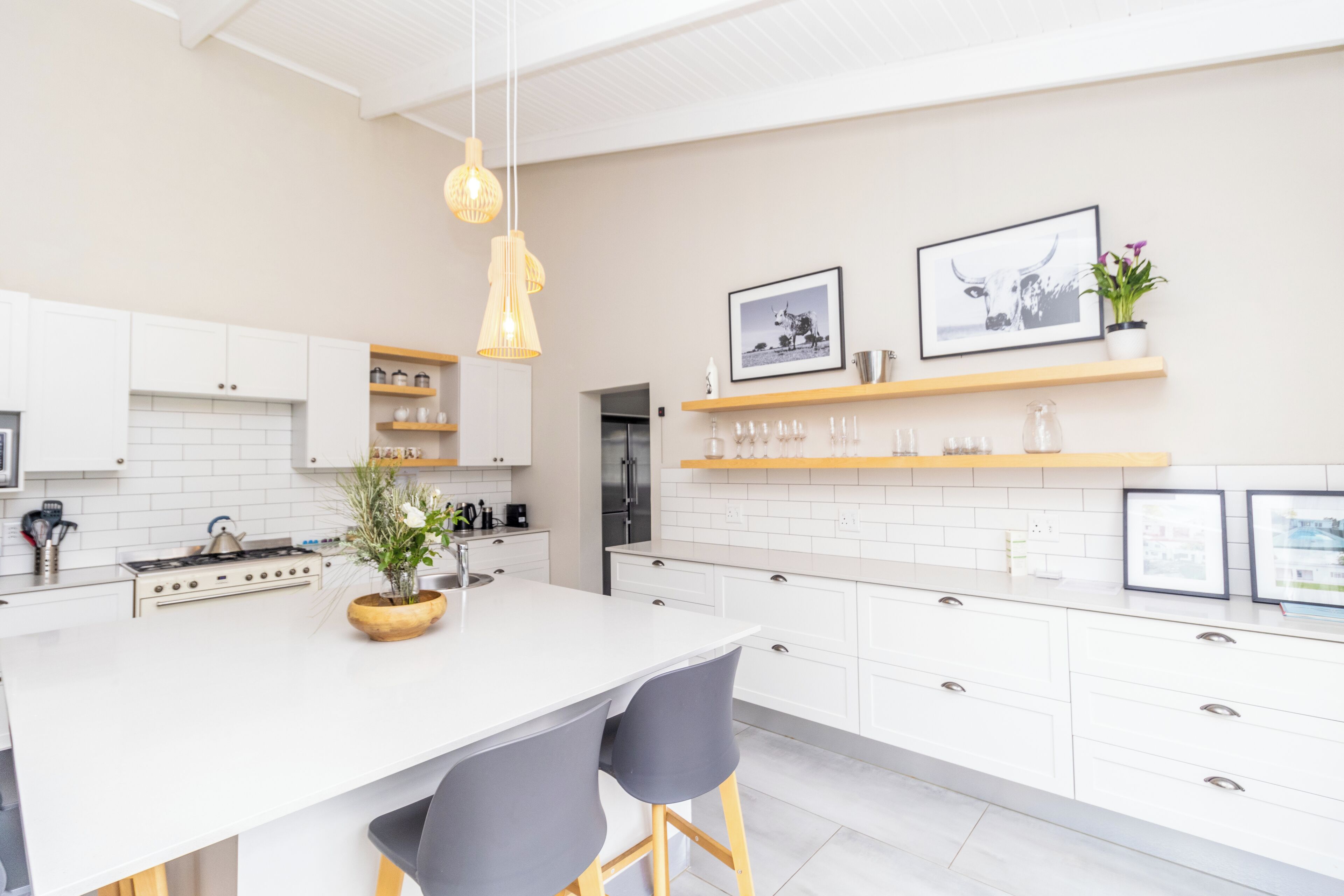 A modern kitchen with white cabinets, a central island, pendant lighting, and decorative items on shelves.