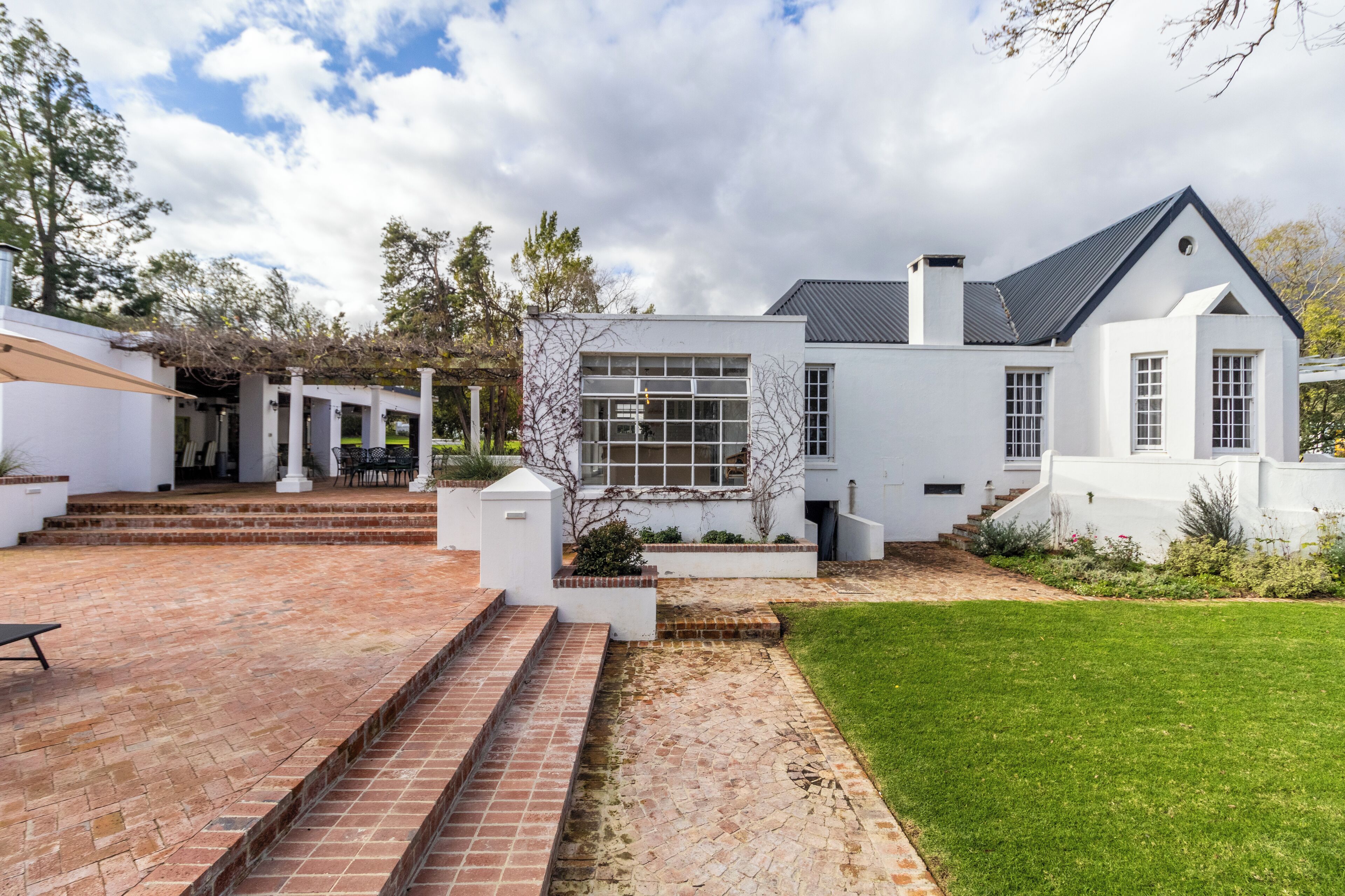 A modern white house with a brick patio, a large window, and a well-maintained lawn.