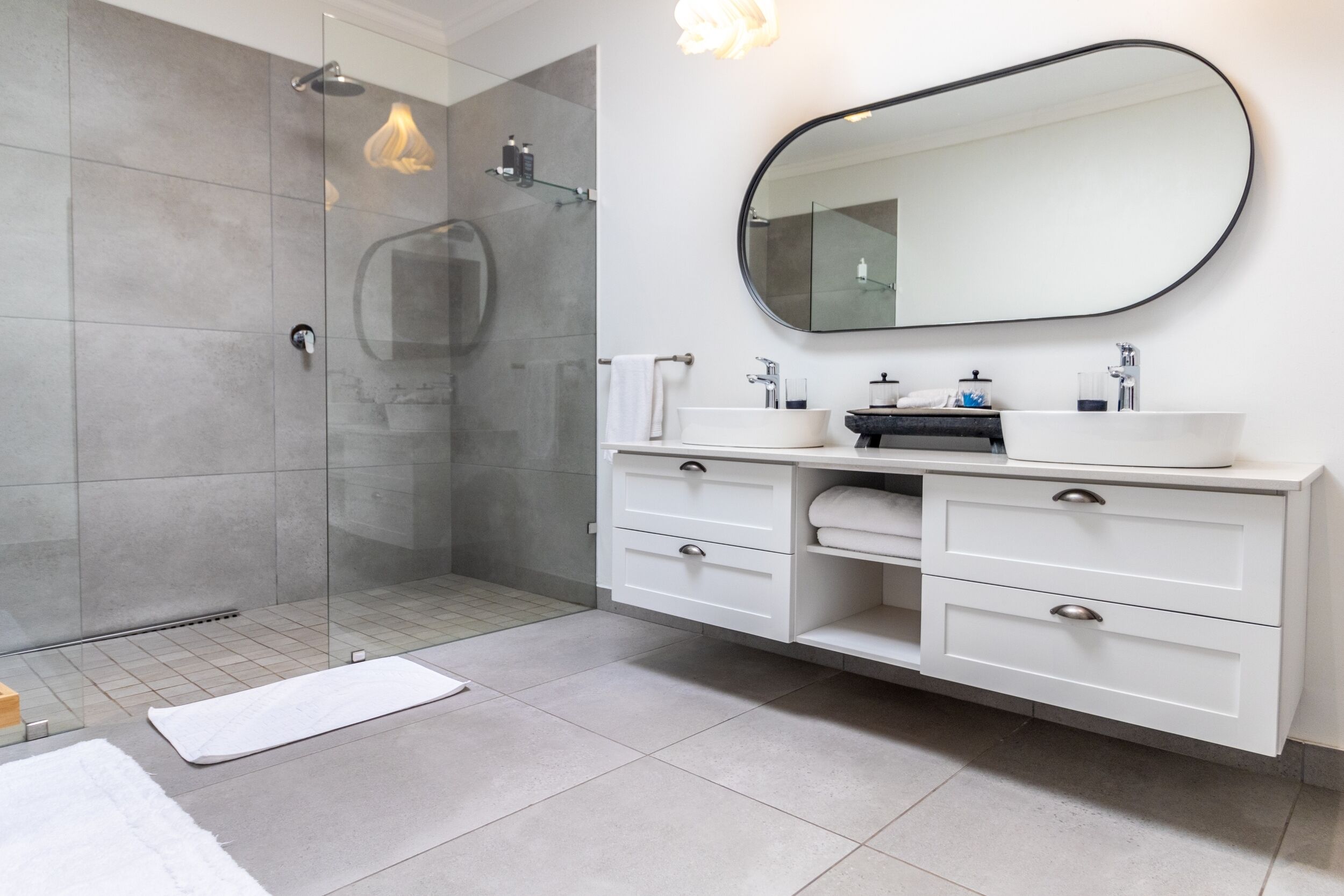 Un baño moderno con ducha de vidrio, tocador blanco con dos lavamanos y un espejo grande.
