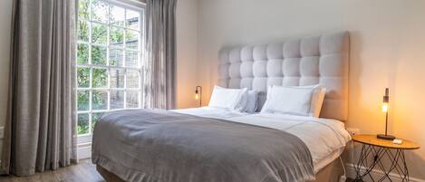 A bedroom with a large bed, a window with curtains, a bedside lamp, and an air conditioning unit.