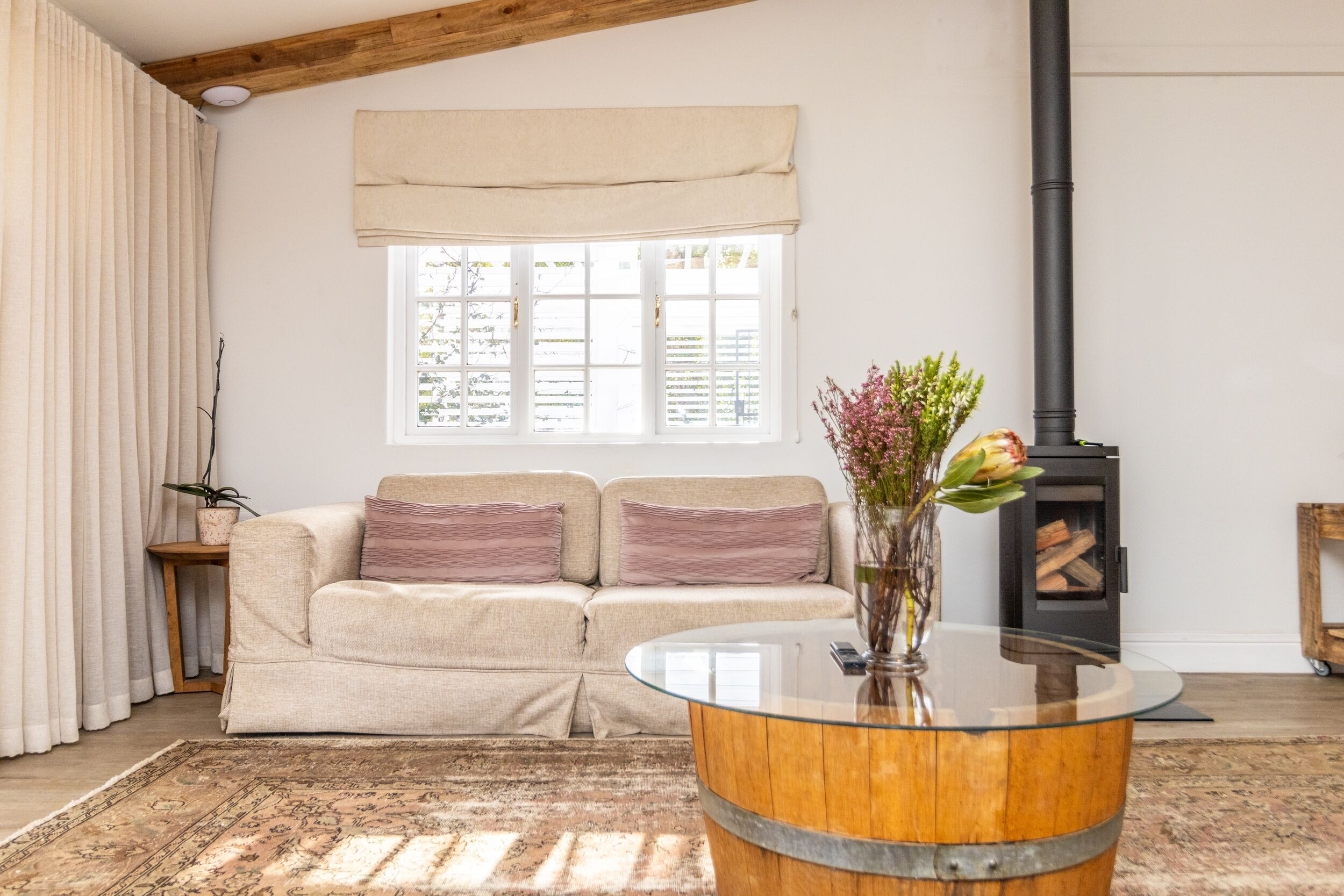 Una sala de estar acogedora con un sofá color beige, una mesa de centro de vidrio, una chimenea y un ventanal con cortinas.