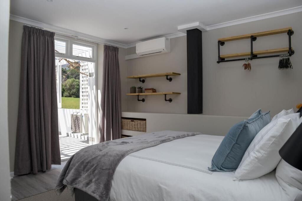 A bedroom with a bed, a window with curtains, a wall-mounted shelf, and an air conditioning unit.