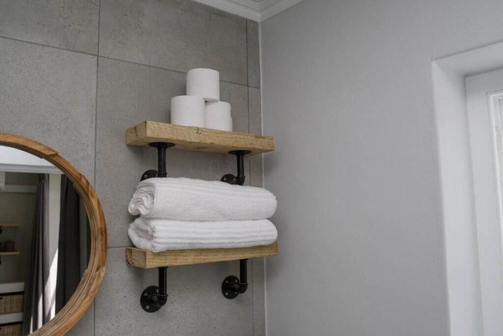A bathroom with a wooden towel rack holding rolled towels and toilet paper.
