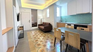 A modern kitchen with a tiled backsplash, a dining area with a table and chairs, a sofa, and a television mounted on the wall.