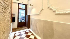 A hallway with a checkered floor, a door with a view of the outside, and decorative wall moldings.
