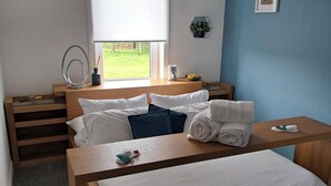 A modern bedroom with a bed, a wooden nightstand, a bedside table, and a window with a view of a green lawn. - Apartment - Sleeps 4 - Pet Friendly - Parking (Troon)