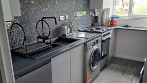 A compact kitchen with a built-in washing machine, a dish rack, and a window providing natural light. - Apartment - Sleeps 4 - Pet Friendly - Parking (Troon)