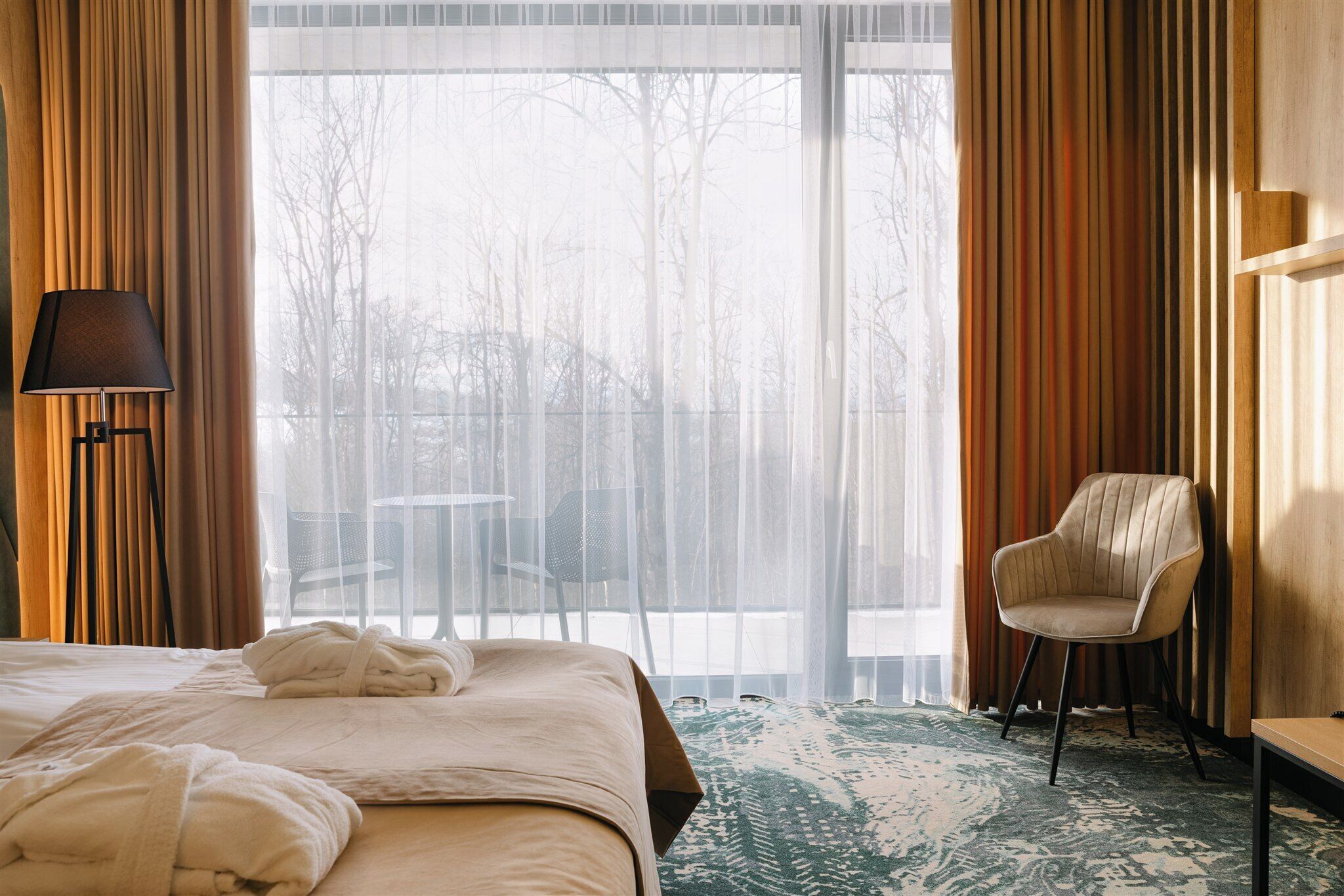 A hotel room with a bed, a chair, a table, and a lamp.