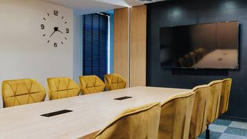 A conference room with a long table, yellow chairs, a clock, and a TV on the wall.