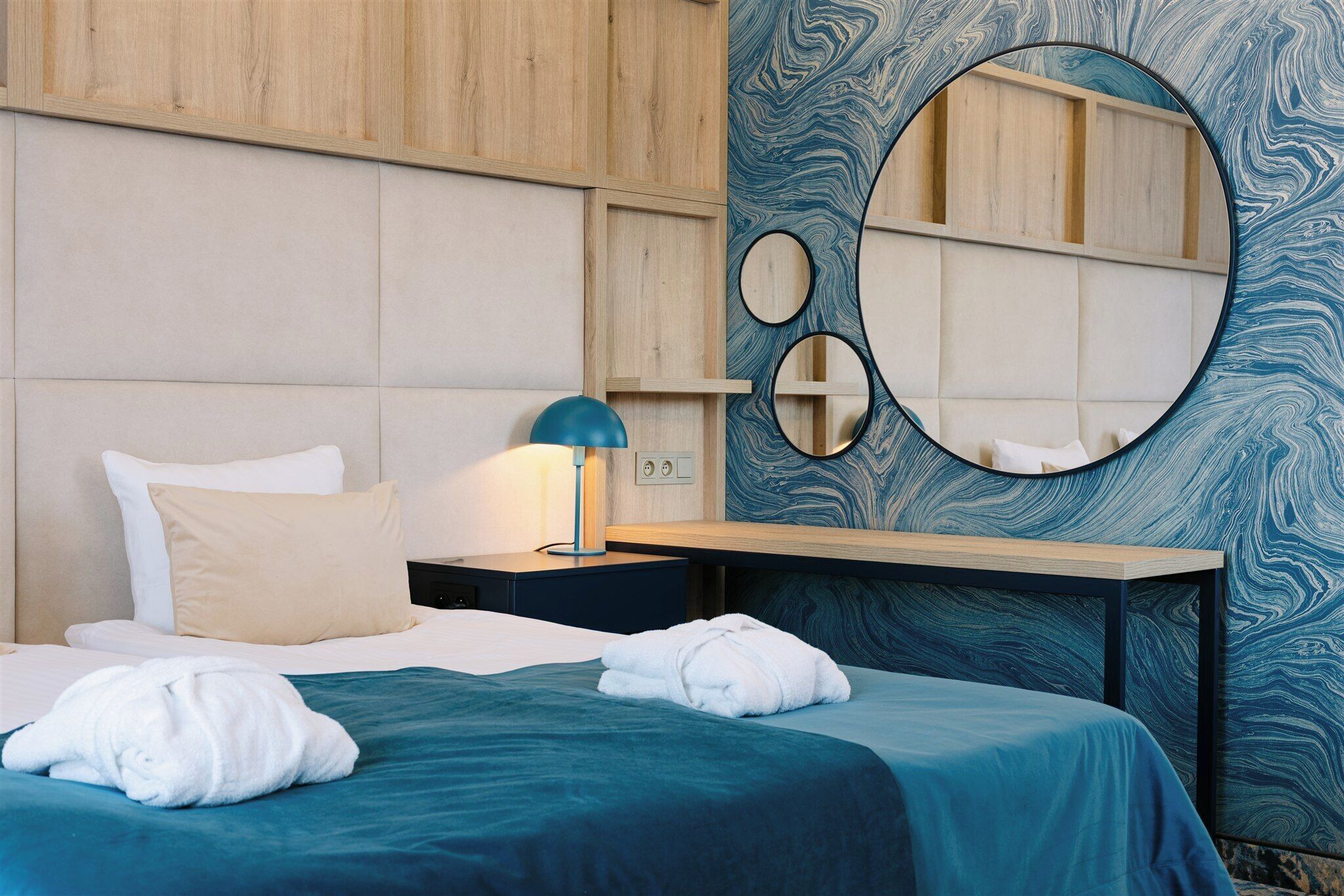 A hotel room with a bed, a nightstand, a lamp, and a wall with a large mirror and decorative circles.