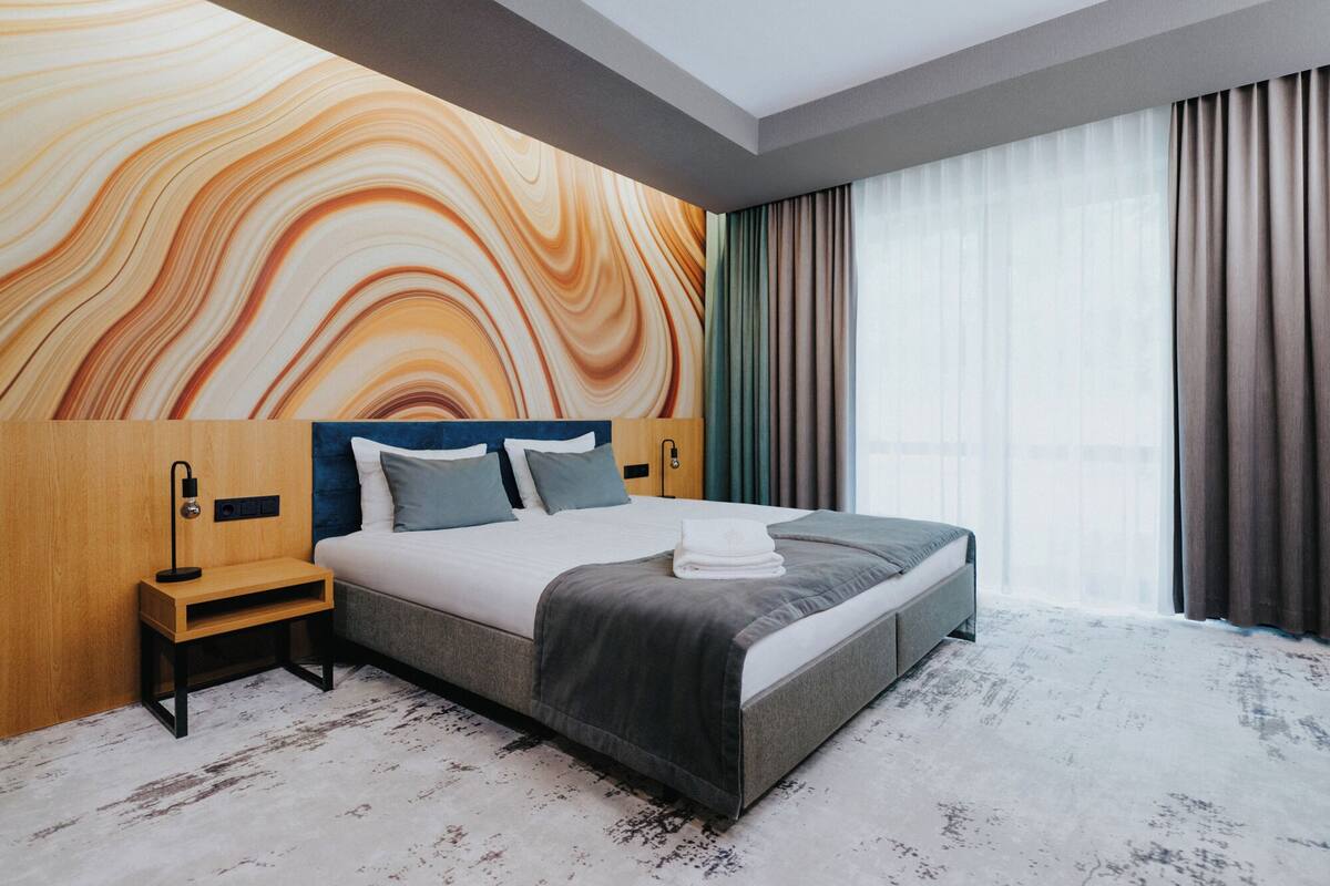Une chambre d’hôtel moderne avec un grand lit, une tête de lit en bois, une table de chevet et une fresque murale.