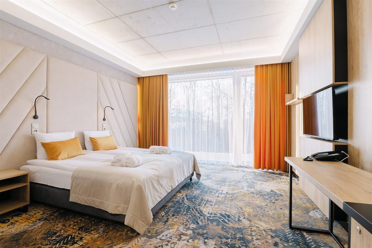 Une chambre d’hôtel avec un lit, un bureau, une télévision et une grande fenêtre avec des rideaux.
