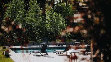 Zona junto a la piscina con sillones de descanso y una mesita, rodeada de vegetación.