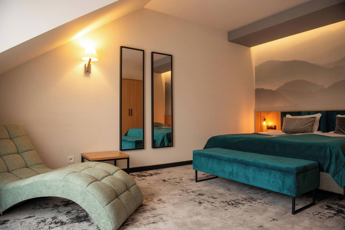 Une chambre à coucher moderne avec un lit, un banc, une chaise et deux miroirs.