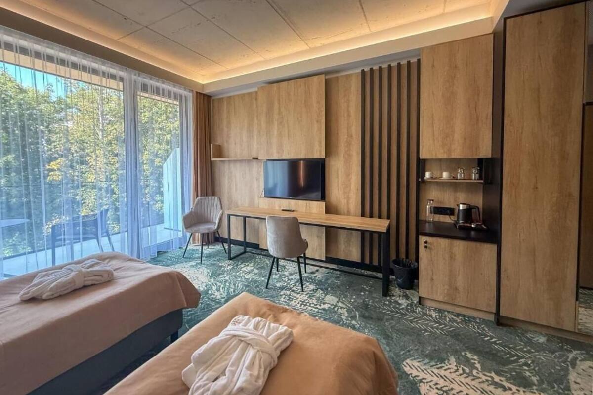 Une chambre d’hôtel moderne dotée d’un grand lit, d’un bureau avec une télévision et offrant une vue sur les arbres à travers de grandes fenêtres.