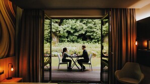 A room with a bed, a dining table with chairs, and a view of a garden through an open door. - Aspen Prime Ski & Bike Resort (Podlesie)