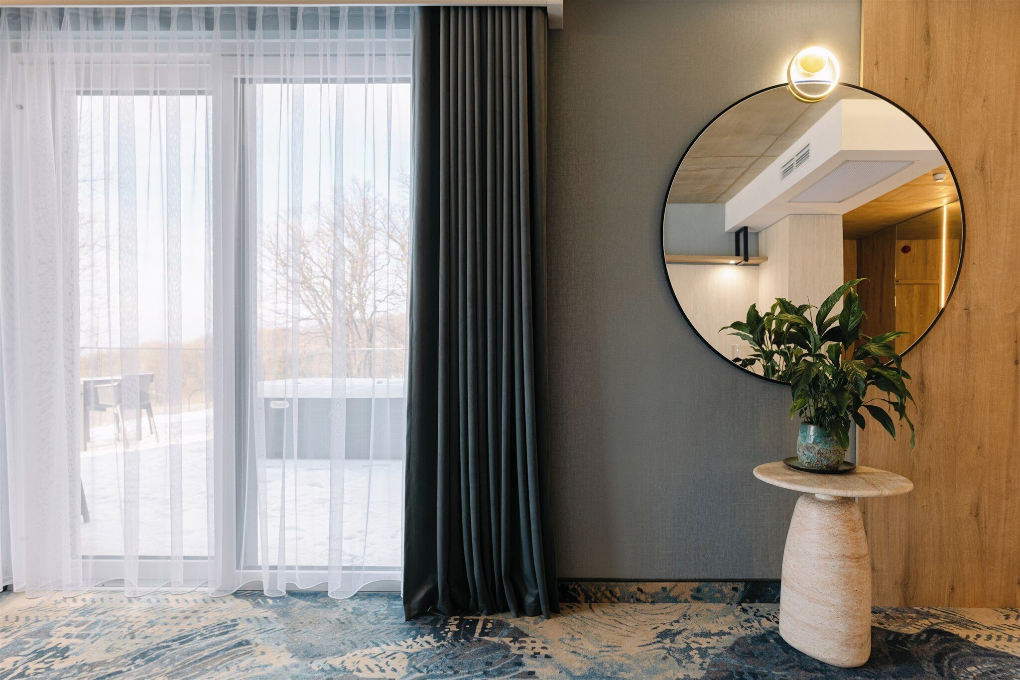Une pièce dotée d’une grande fenêtre, d’un miroir, d’une plante en pot et d’un tapis à motifs.