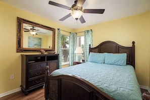 A bedroom with a bed, a dresser, a ceiling fan, a mirror, and a window with curtains.