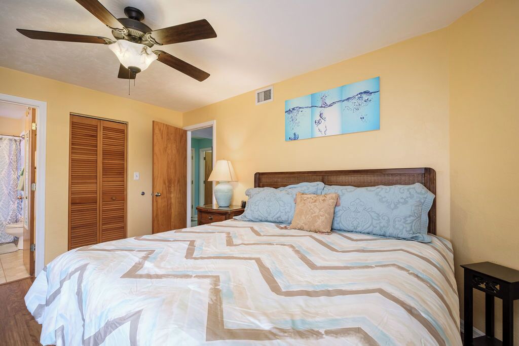 A bedroom with a bed, wooden wardrobe, ceiling fan, and a wall painting.