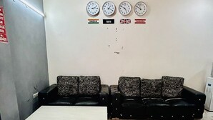 Ein Wartebereich mit einer Sofagruppe, einem Couchtisch und Uhren, die Zeiten aus verschiedenen Ländern anzeigen.