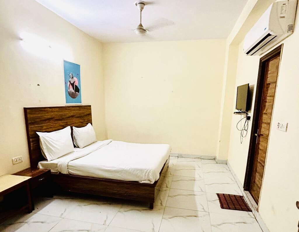 Une chambre à coucher avec un lit, un ventilateur de plafond, un climatiseur, une télévision et une porte.