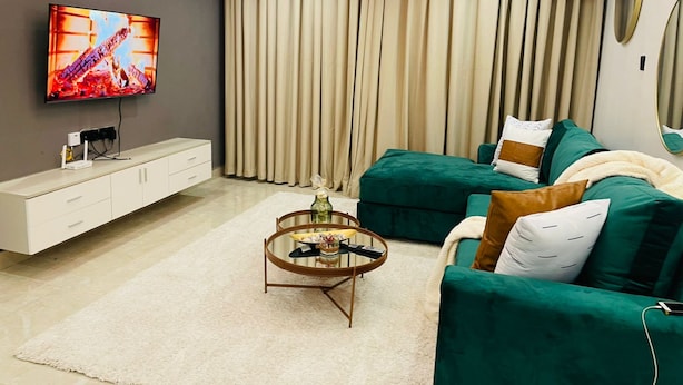 Un salon moderne avec un téléviseur, un canapé, une table basse et une grande fenêtre avec des rideaux.