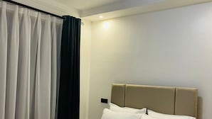Un lit bien fait, avec une tête de lit, un rideau blanc et un luminaire visible au plafond.