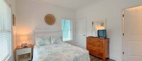 A bedroom with a bed, a dresser, a ceiling fan, a window with blinds, and a wall-mounted round mirror.