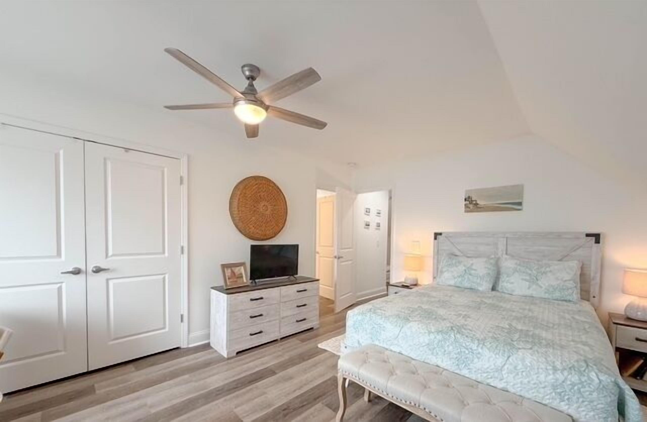A bedroom with a bed, a ceiling fan, a dresser, and a door.
