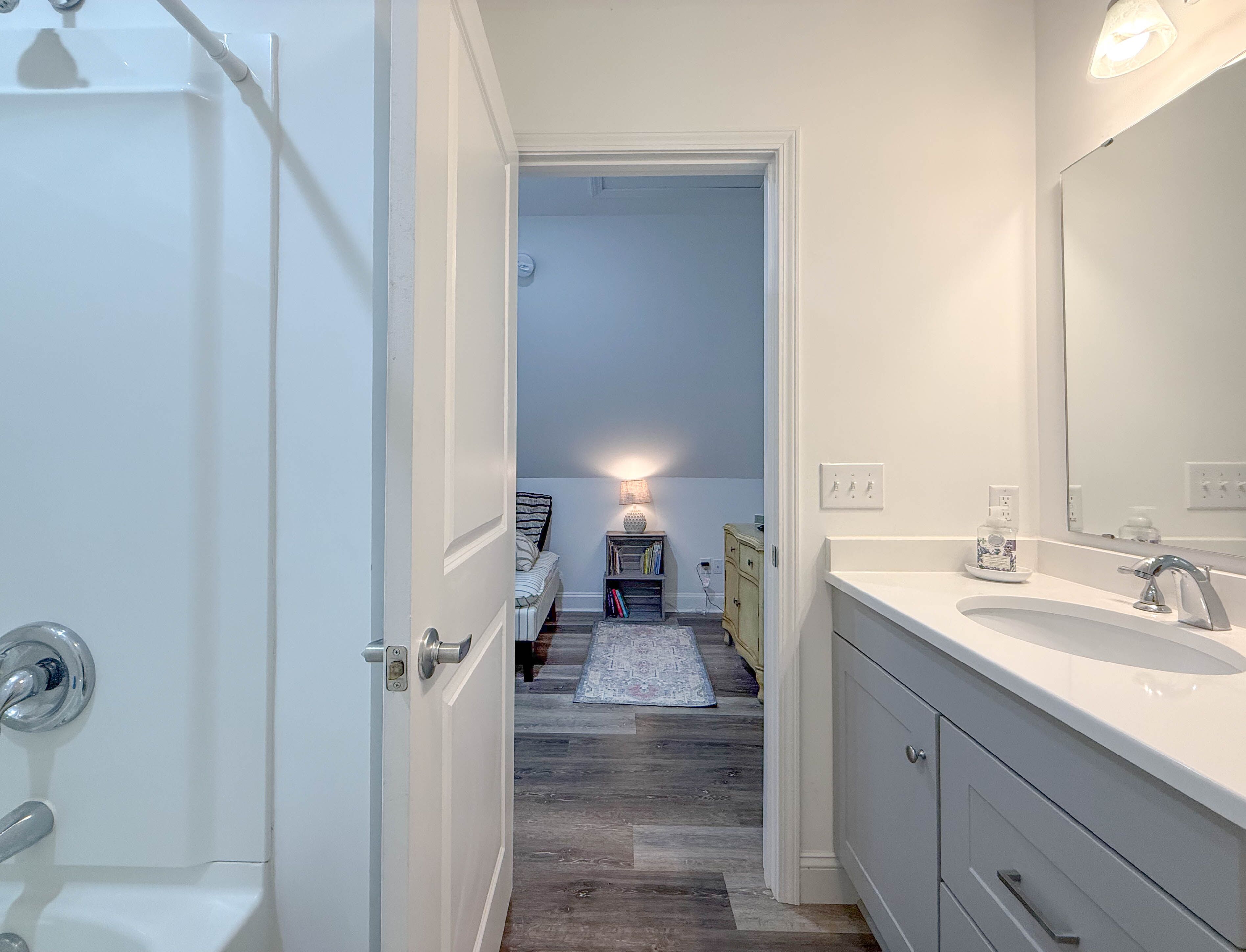 Un baño con un lavamanos blanco, un espejo y una puerta que da a un dormitorio.