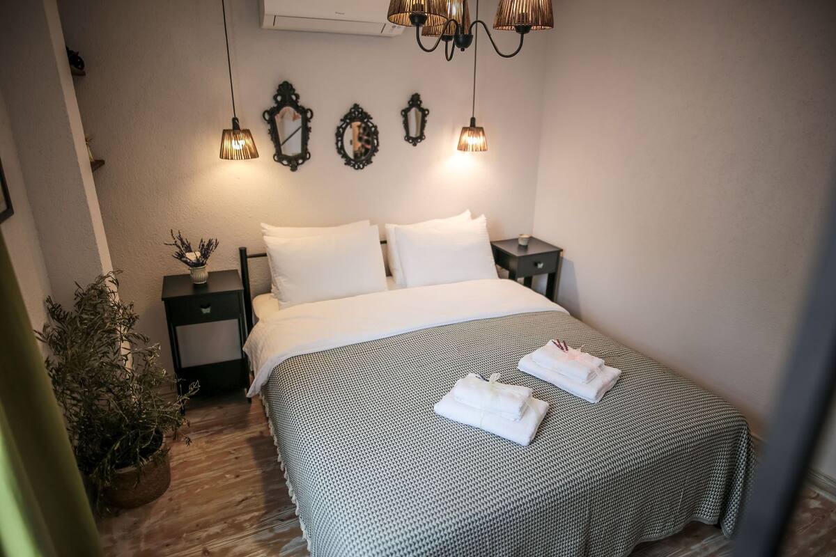 A neatly made bed with a patterned bedspread, two bedside tables with lamps, a potted plant, and decorative mirrors on the wall.