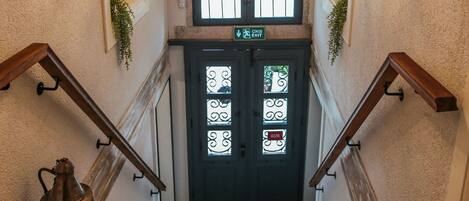 A wooden staircase with a black door at the top, a hanging lantern, and decorative plates on the walls.