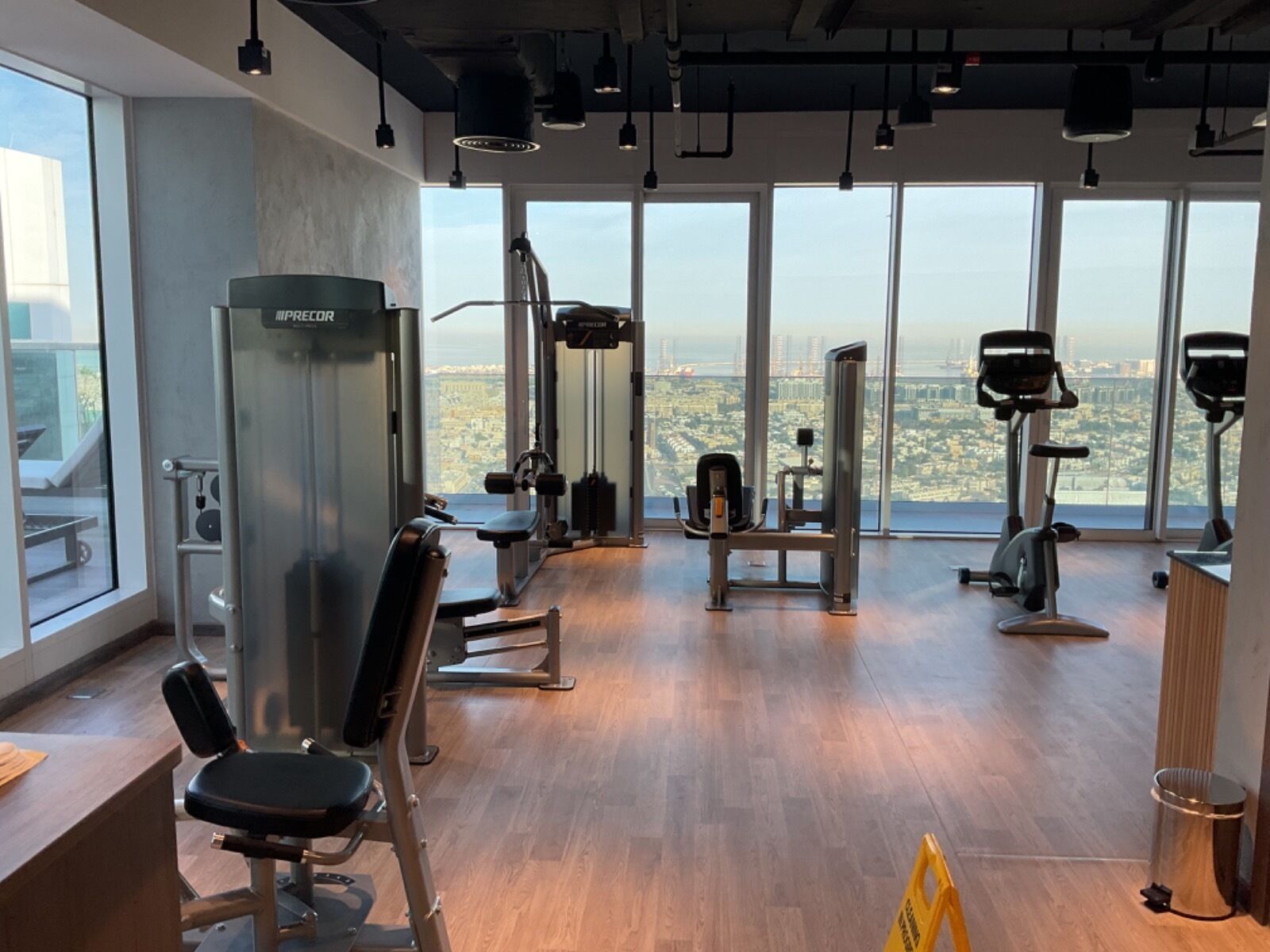 Ein Fitnessstudio mit diversen Trainingsgeräten, großen Fenstern und Blick auf die Stadt.