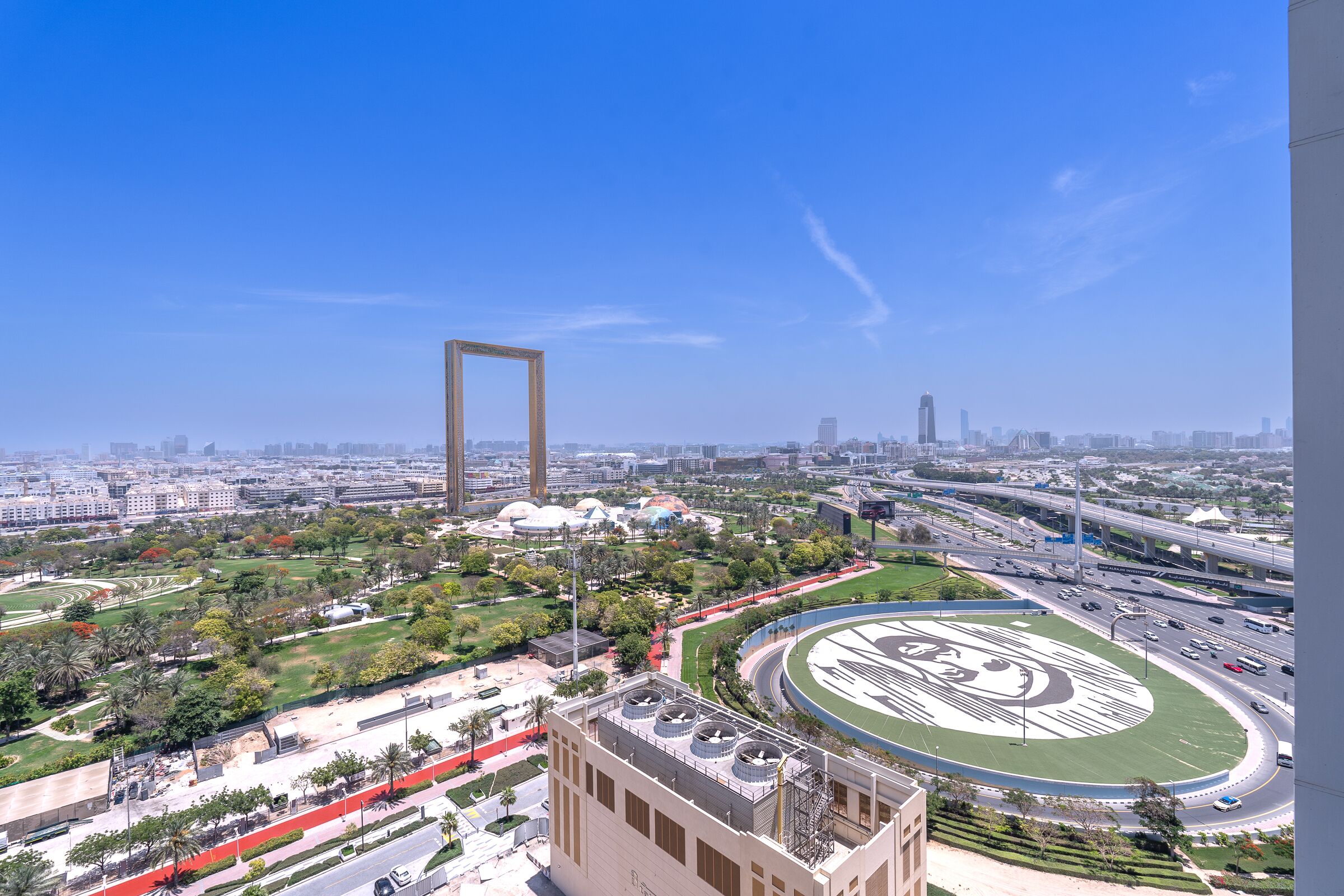 A cityscape with a large open plaza, a circular park with a central design, and a modern building with a unique facade.