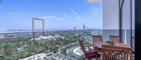 A balcony with a table and chairs, offering a view of a cityscape and greenery below.