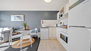 A modern kitchen with white cabinetry, a dishwasher, and a microwave. There is a dining area with a table and chairs, and a small rug on the floor.