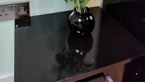 Een zwarte vaas met witte bloemen op een zwarte tafel, voor een lichtgroene muur.