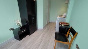 Een kleine kamer met een zwarte garderobe, een tafeltje met een mandje en een stoel.