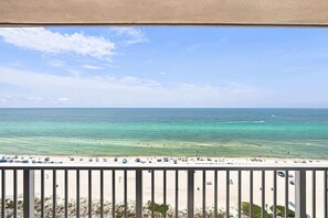 Une vue sur la plage depuis un balcon doté d’une balustrade, avec un ciel dégagé et une mer calme.