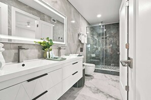 A modern bathroom with a large mirror, a white vanity, a shower area, and a glass door leading to a balcony.