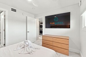 A modern hotel room with a bed, a wooden dresser, a television displaying 'FUNQUEST Vacation Rentals', and a laundry area. - The Summit 1512 - Your Ultimate Vacation Retreat! (Panama City)