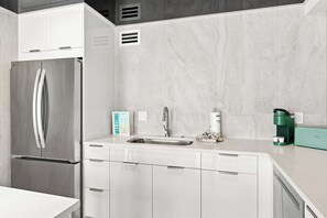 Una cocina moderna con un refrigerador de acero inoxidable, un lavamanos con grifo y una cafetera sobre la encimera.