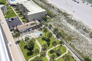 A hotel with a swimming pool, palm trees, and a beach view.