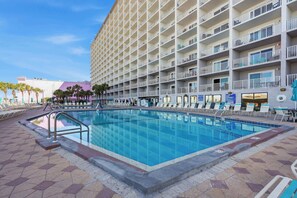 Un hotel con una piscina grande, varios balcones y un cielo despejado.