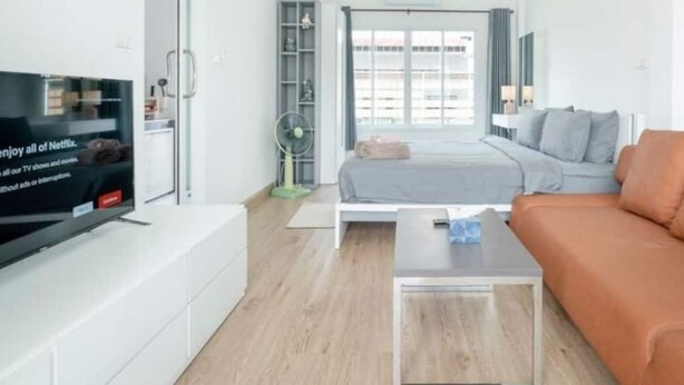 A modern living room with a flat-screen TV, a sofa, a bed, and a coffee table. - Charming Studio Suite - Private Washer  (Chalong)
