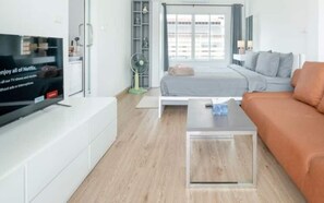 Ein modernes Wohnzimmer mit Flachbildfernseher, einer Couch, einem Bett und einem Couchtisch.