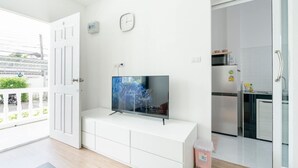 A modern apartment with a large TV on a white cabinet, a kitchen with stainless steel appliances, and a balcony with a white railing. - Charming Studio Suite - Private Washer  (Chalong)